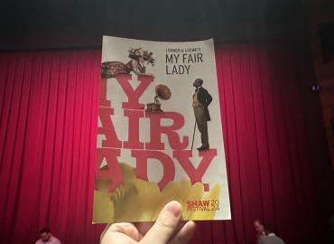 image of the playbill for My Fair Lady, held in front of red theatre curtains