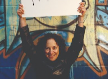 Sali Tagliamonte stands in front of a colorful wall holding a sign that depicts the word &amp;quot;Talk&amp;quot;